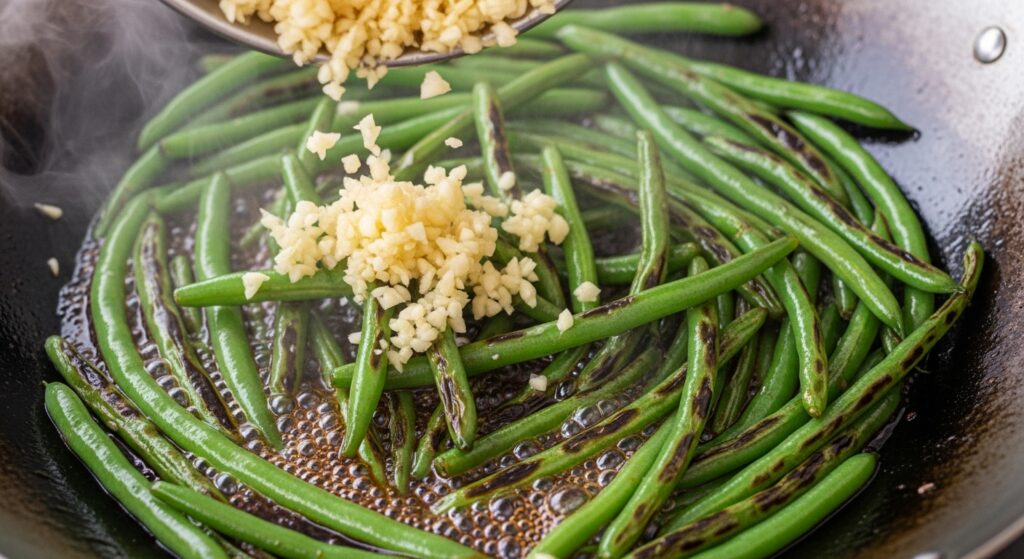 Golden garlic being stir-fried with crispy green beans and glossy soy sauce glaze in a wok.